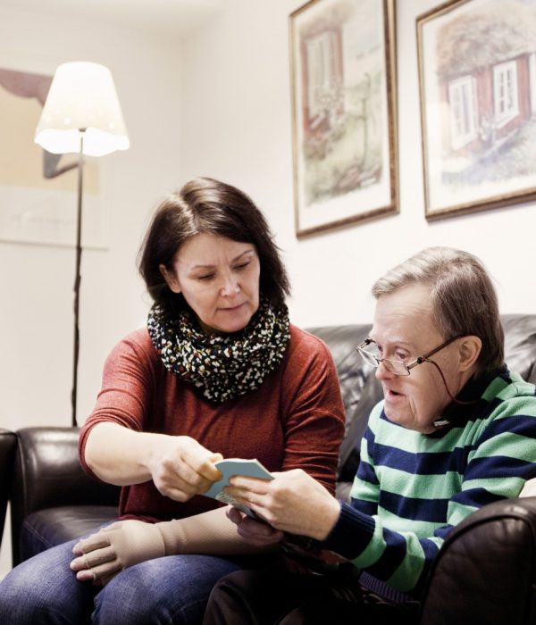 Healthcare worker assisting senior man with down syndrome in reading book